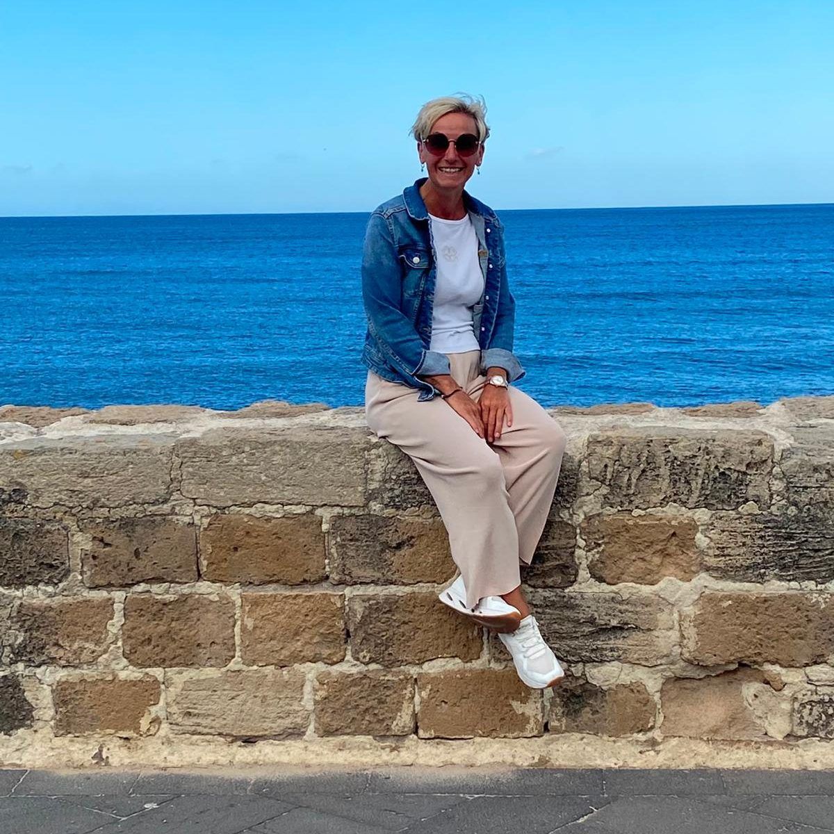 Christiane sitzt auf einer Steinmauer am Meer