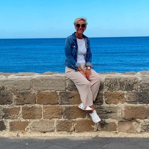 Christiane sitzt auf einer Steinmauer am Meer